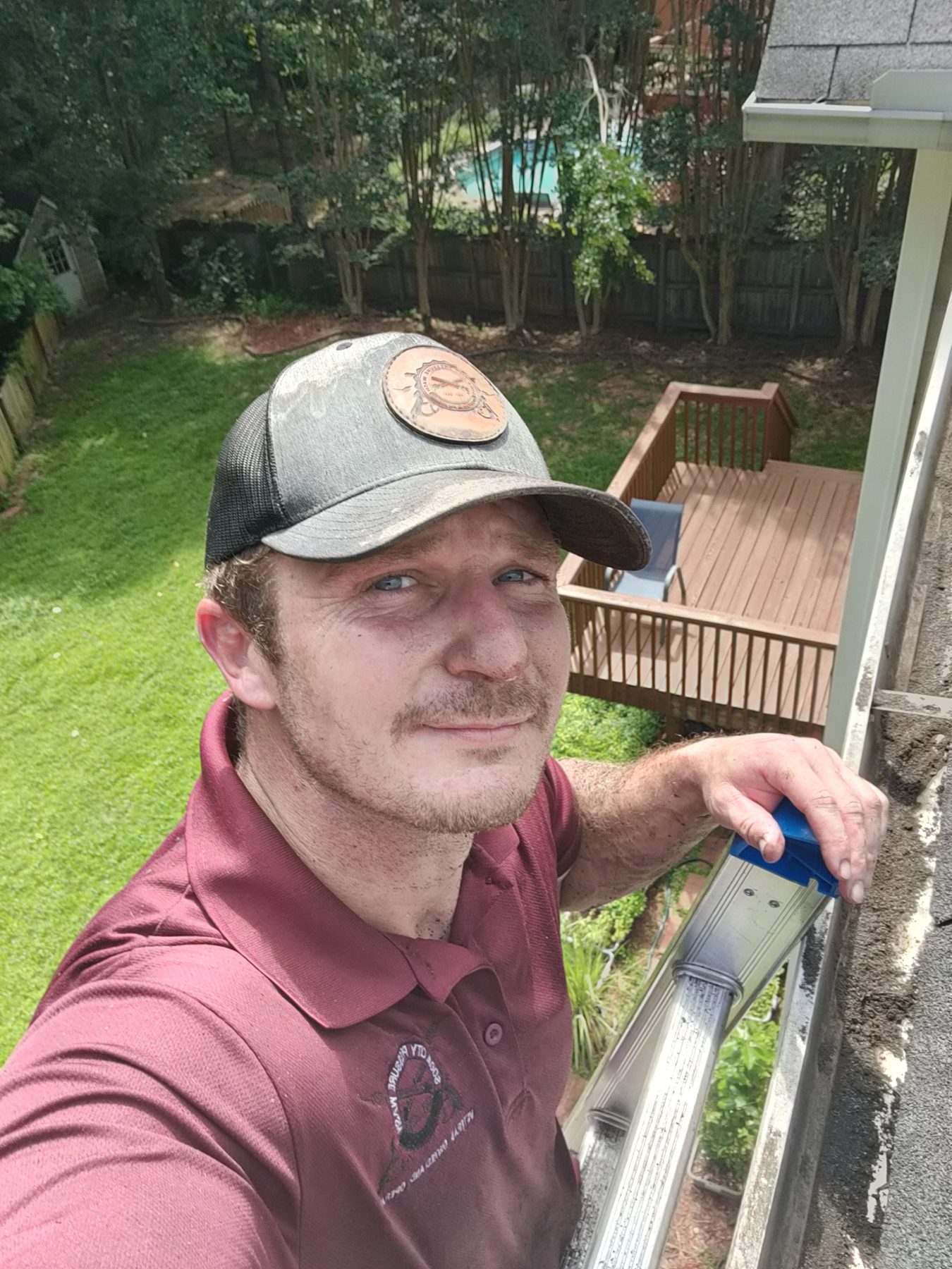 Jeremy on a ladder at the gutter line of a house, deck and lawn behind him