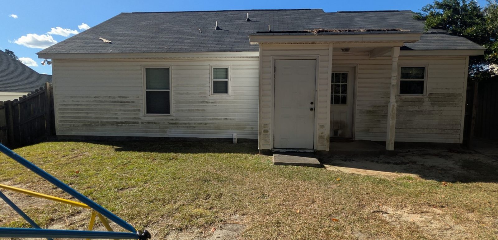 A white vinyl house with green algae along the lower siding, before washing