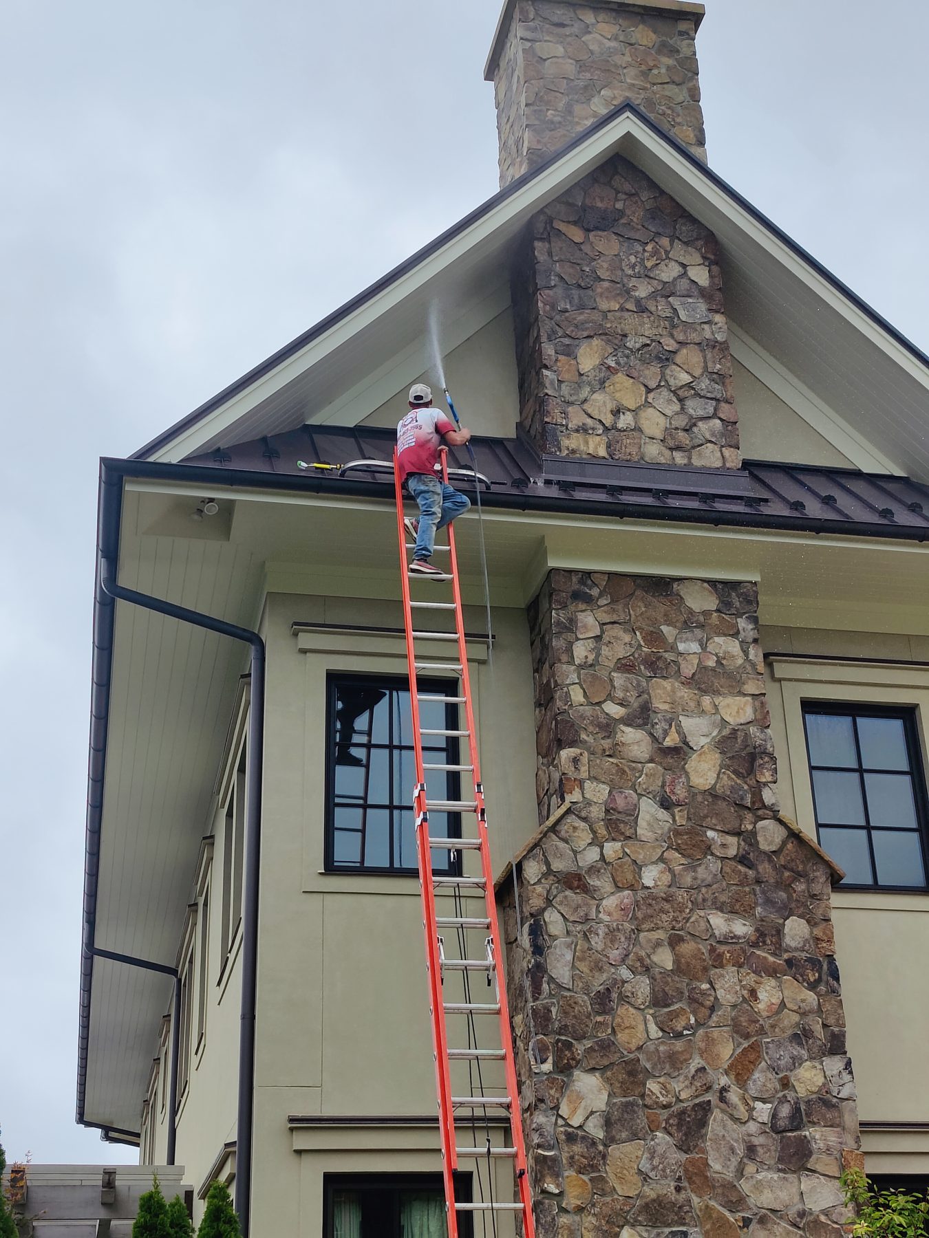 Jeremy on a ladder washing a stone and stucco house